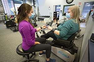 Therapist with a woman using a total body exercise machine in a therapy gym.