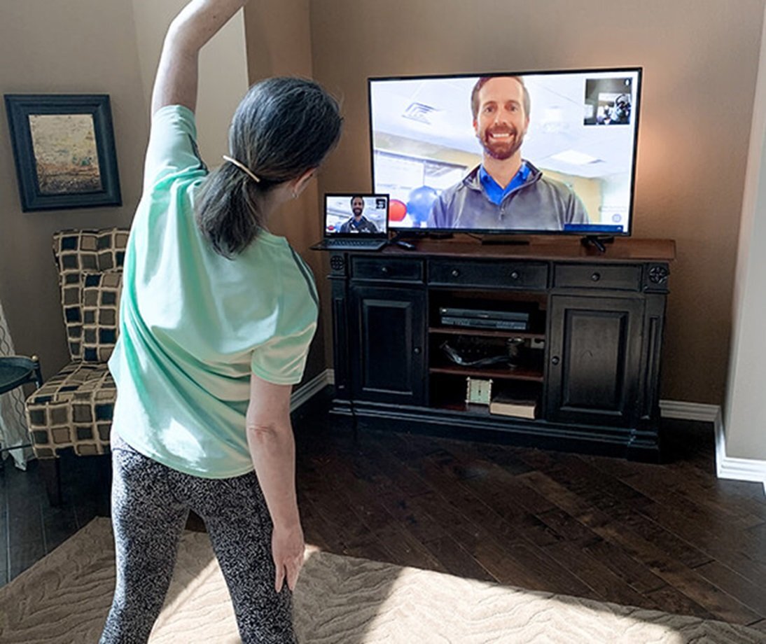 Woman exercsing in her living room using a television to get instruction from a physical therapist