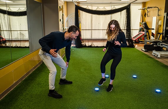 Athlete is about to step on a BlazePod for reaction training drill while a physical therapist is encouraging them